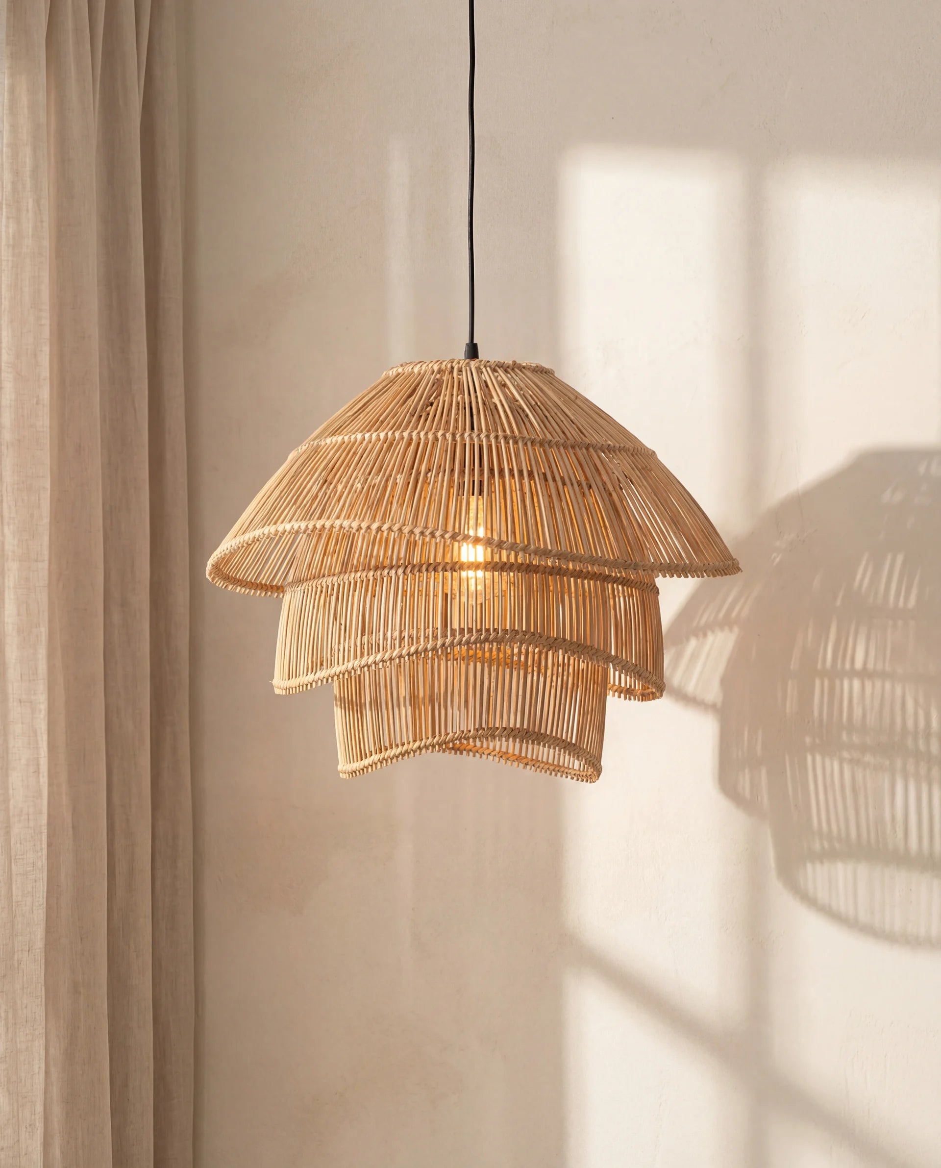 Woven rattan pendant light hanging against a neutral wall with soft shadows.
