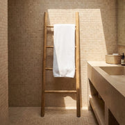 Bathroom with wooden towel ladder and white towel, tiled walls, and a sink.