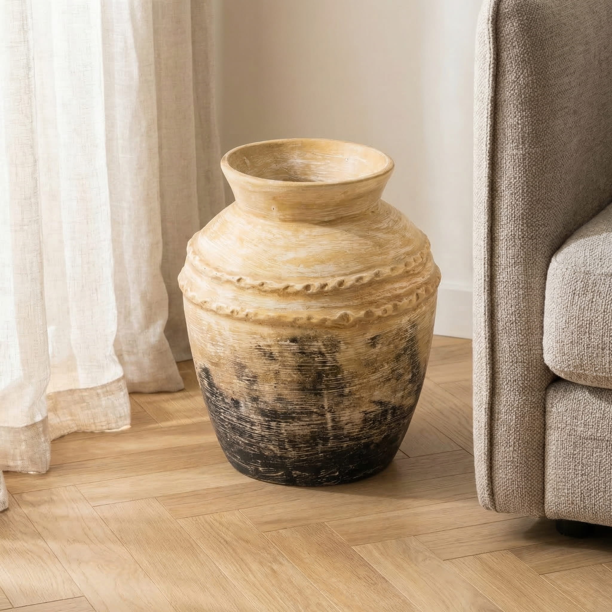 Large ceramic vase on a wooden floor next to a sofa