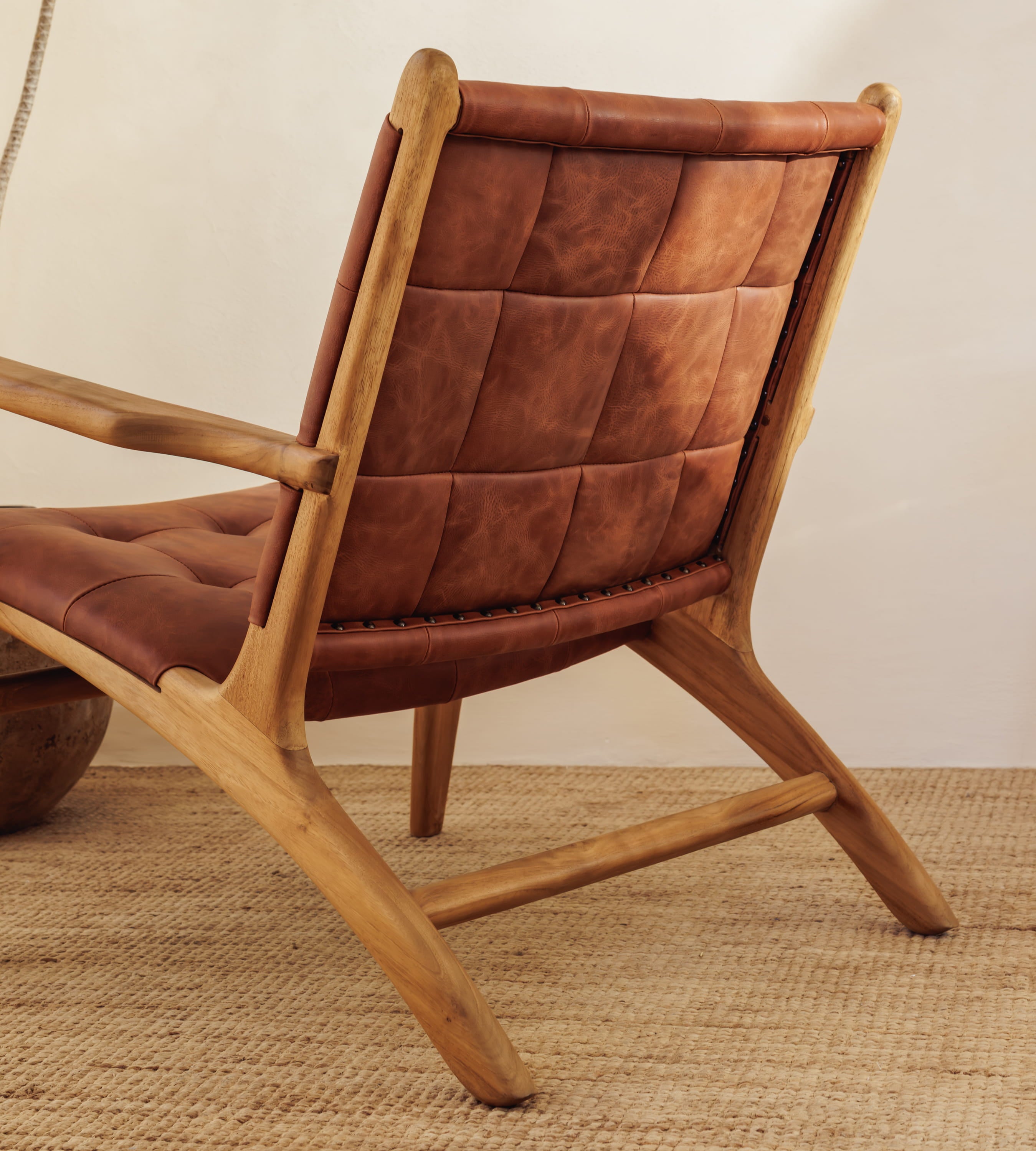 A modern leather armchair with a tufted brown leather sling seat and back, shown in a styled interior setting on a woven rug.