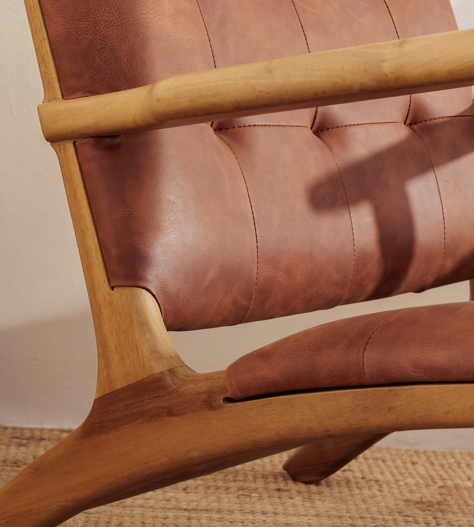 Close-up of a modern leather armchair with tufted brown leather upholstery and a curved natural wood frame.