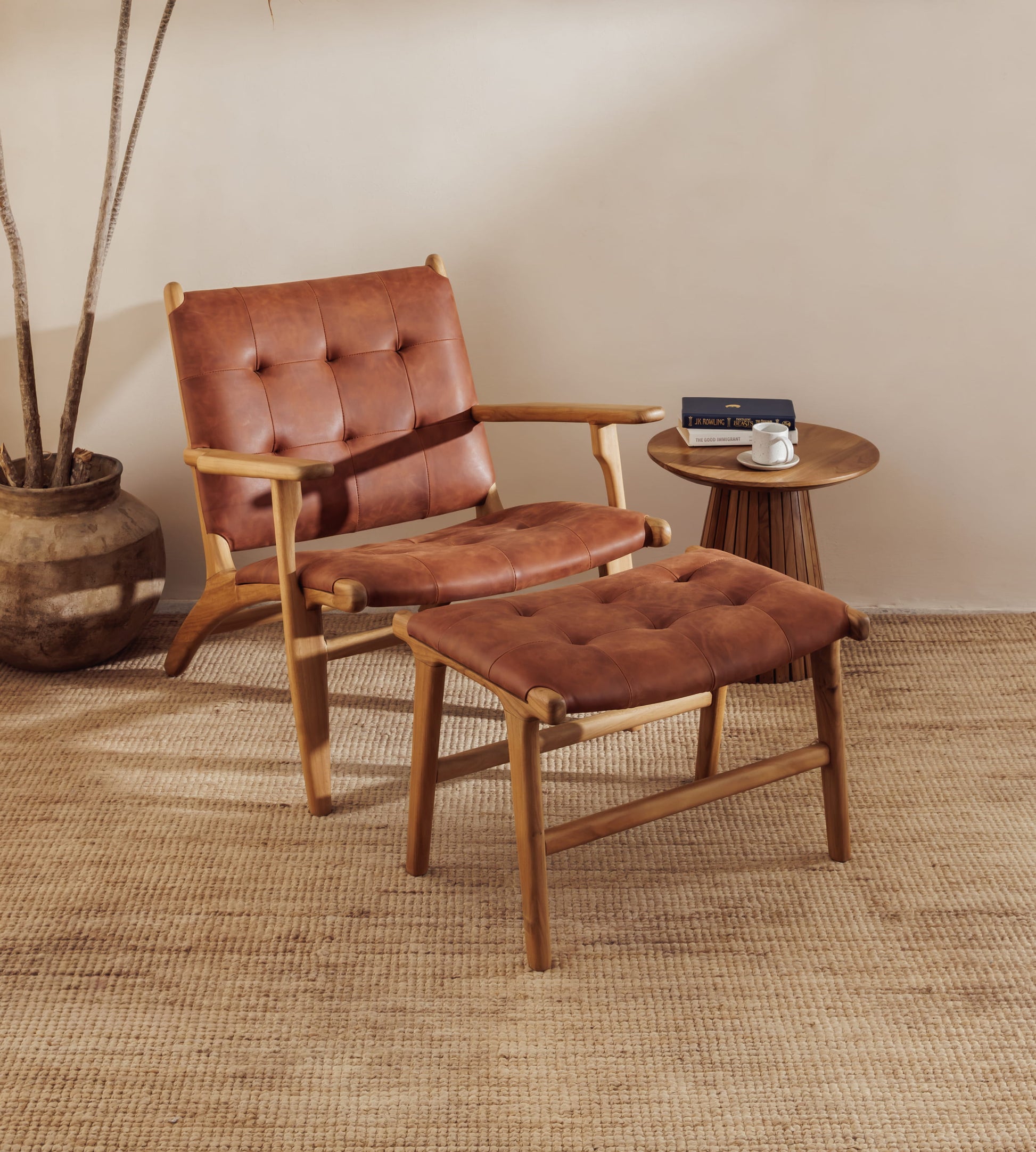A modern leather lounge chair with tufted brown leather upholstery is shown with a matching ottoman in a styled room setting with a side table, woven rug, and potted plant.