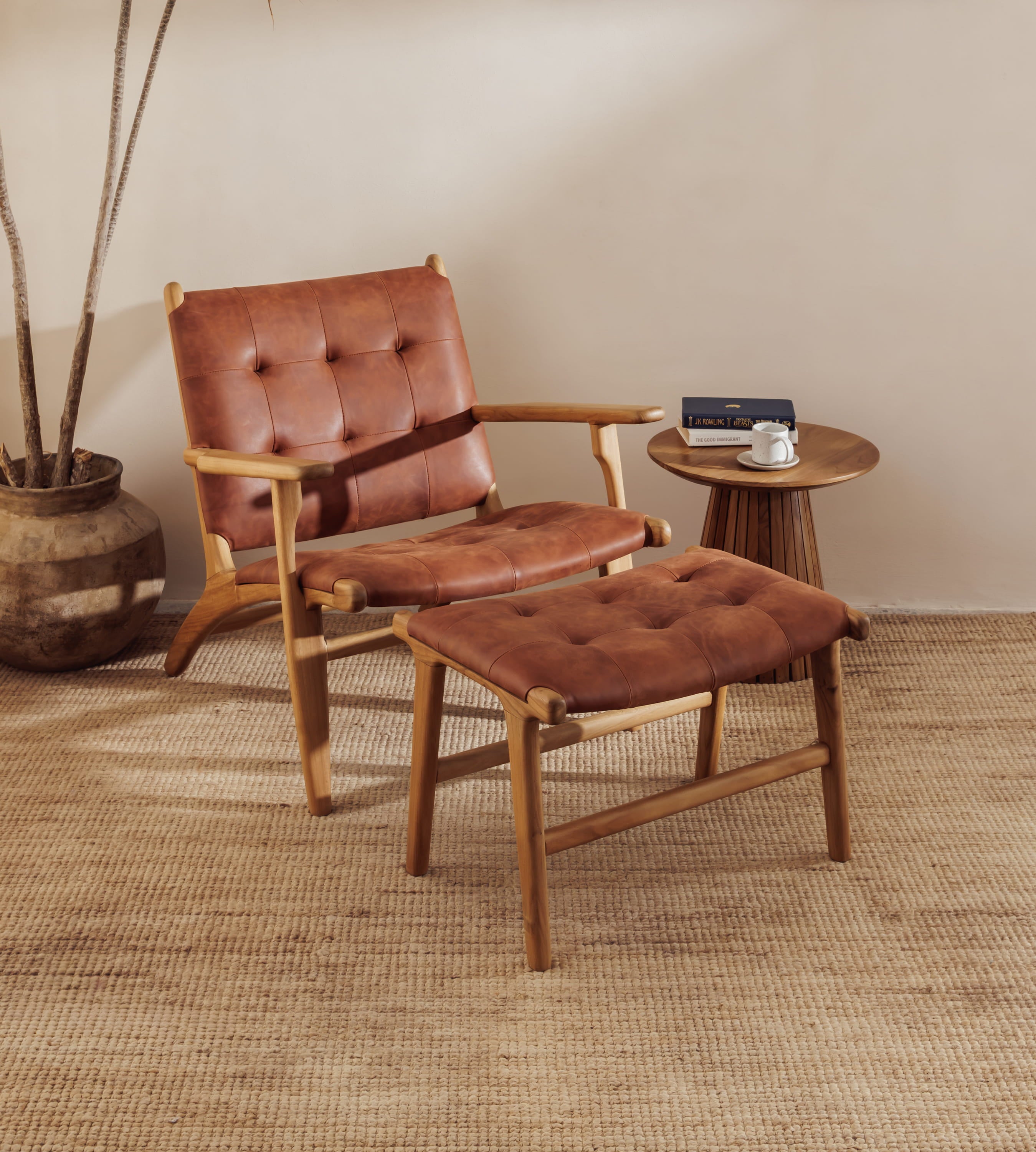 A modern leather lounge chair with tufted brown leather upholstery is shown with a matching ottoman in a styled room setting with a side table, woven rug, and potted plant.