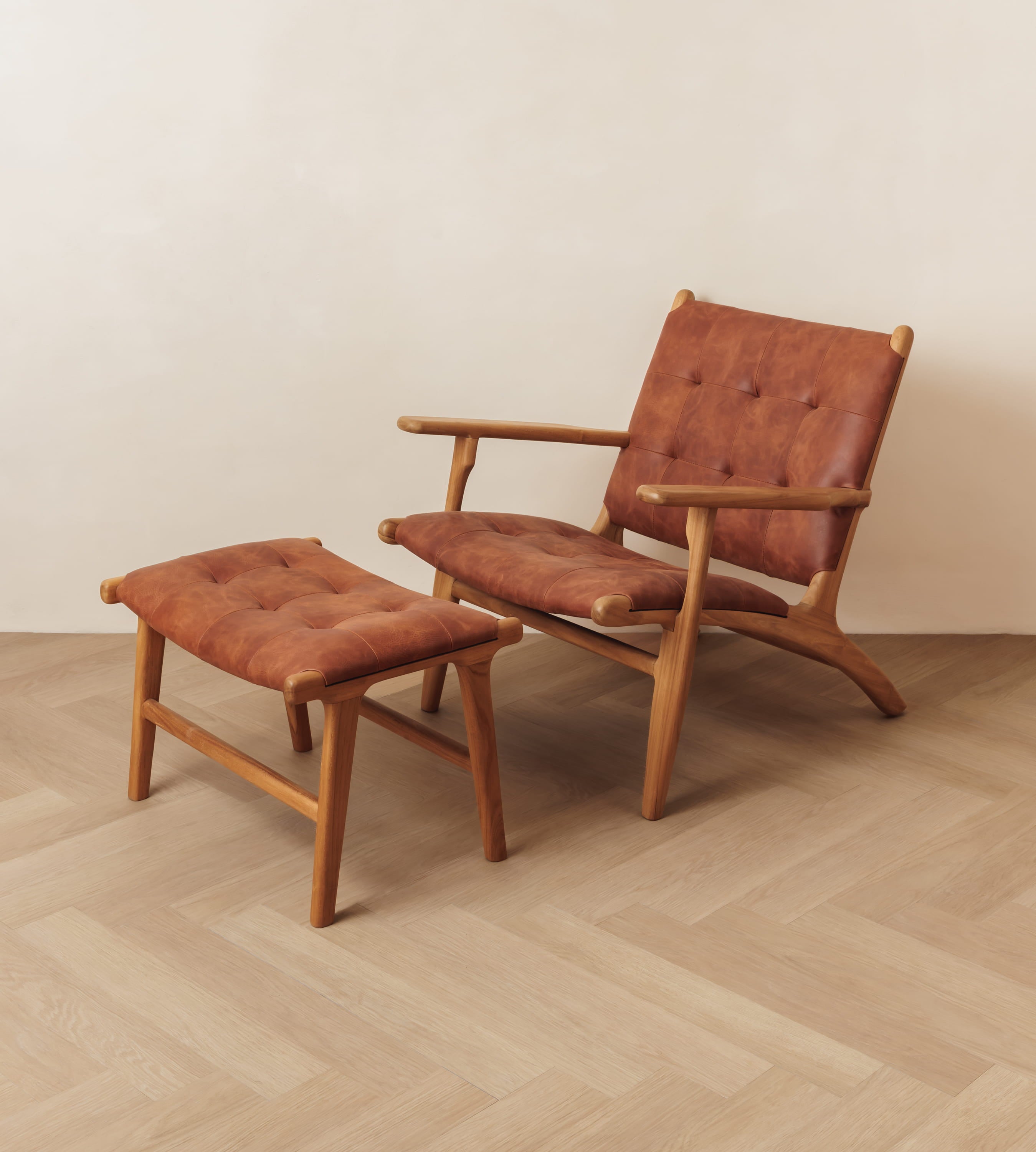 A mid-century modern wooden lounge chair with tufted brown leather upholstery, shown with a matching ottoman on a light wood herringbone floor against a plain beige wall.