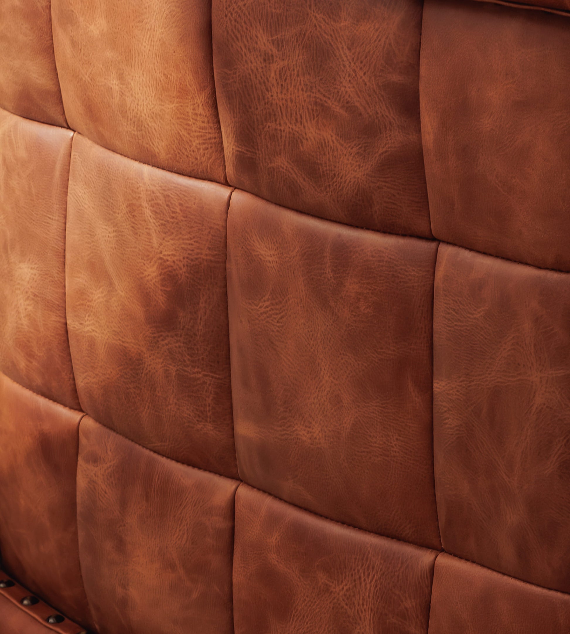 Close-up of a brown leather upholstered surface with a quilted grid pattern and visible leather grain texture.