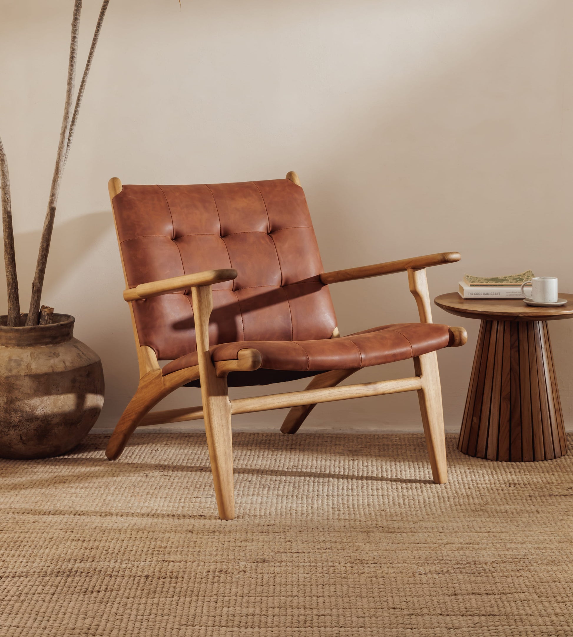 A modern leather accent chair with a brown leather seat and tufted backrest, supported by a curved light wood frame, styled in a room next to a small wooden side table.