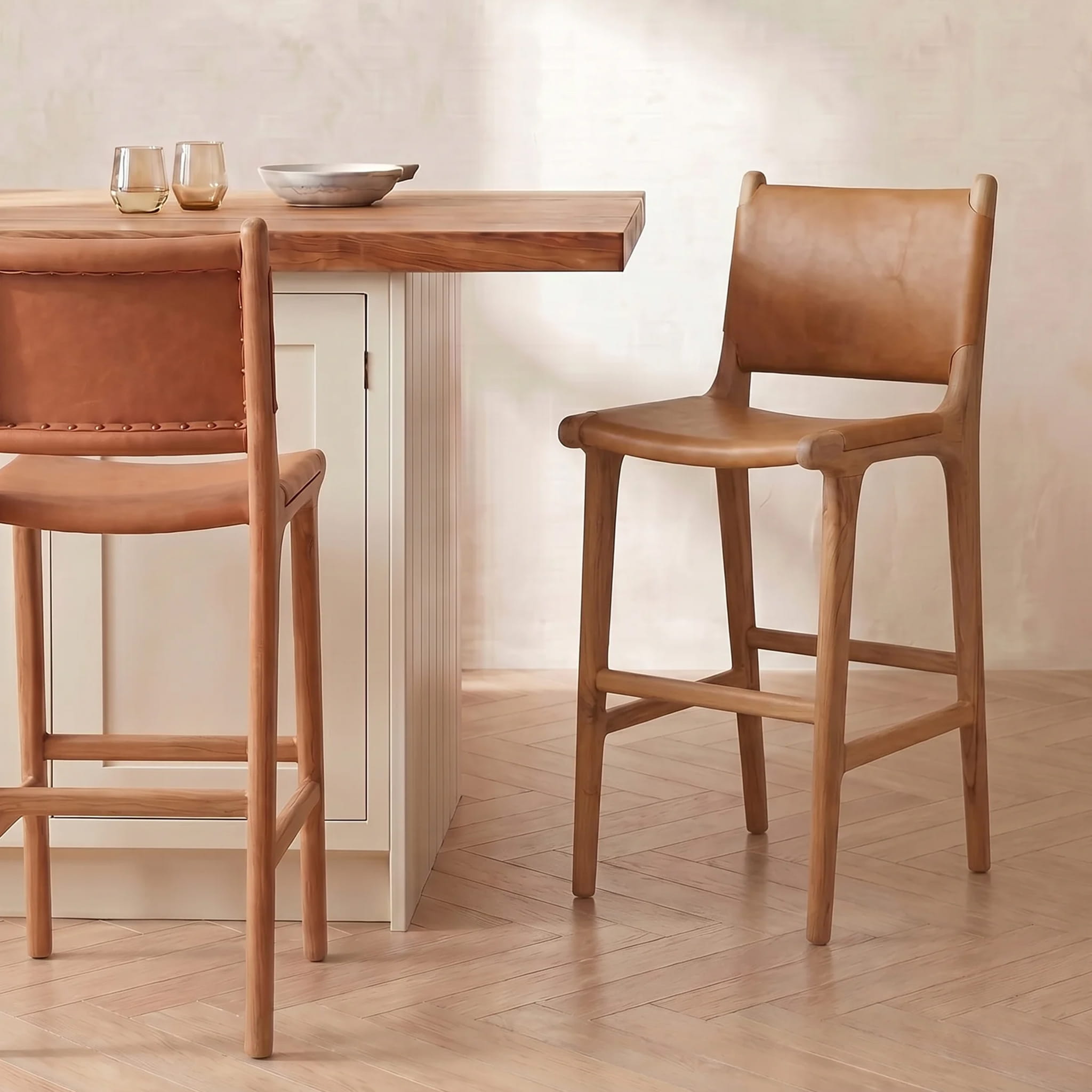 Two brown leather bar stools at a wooden table with a neutral background