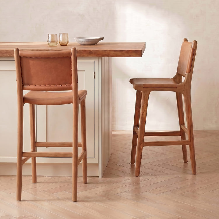 Two wooden bar stools in front of a wooden table with a neutral background.