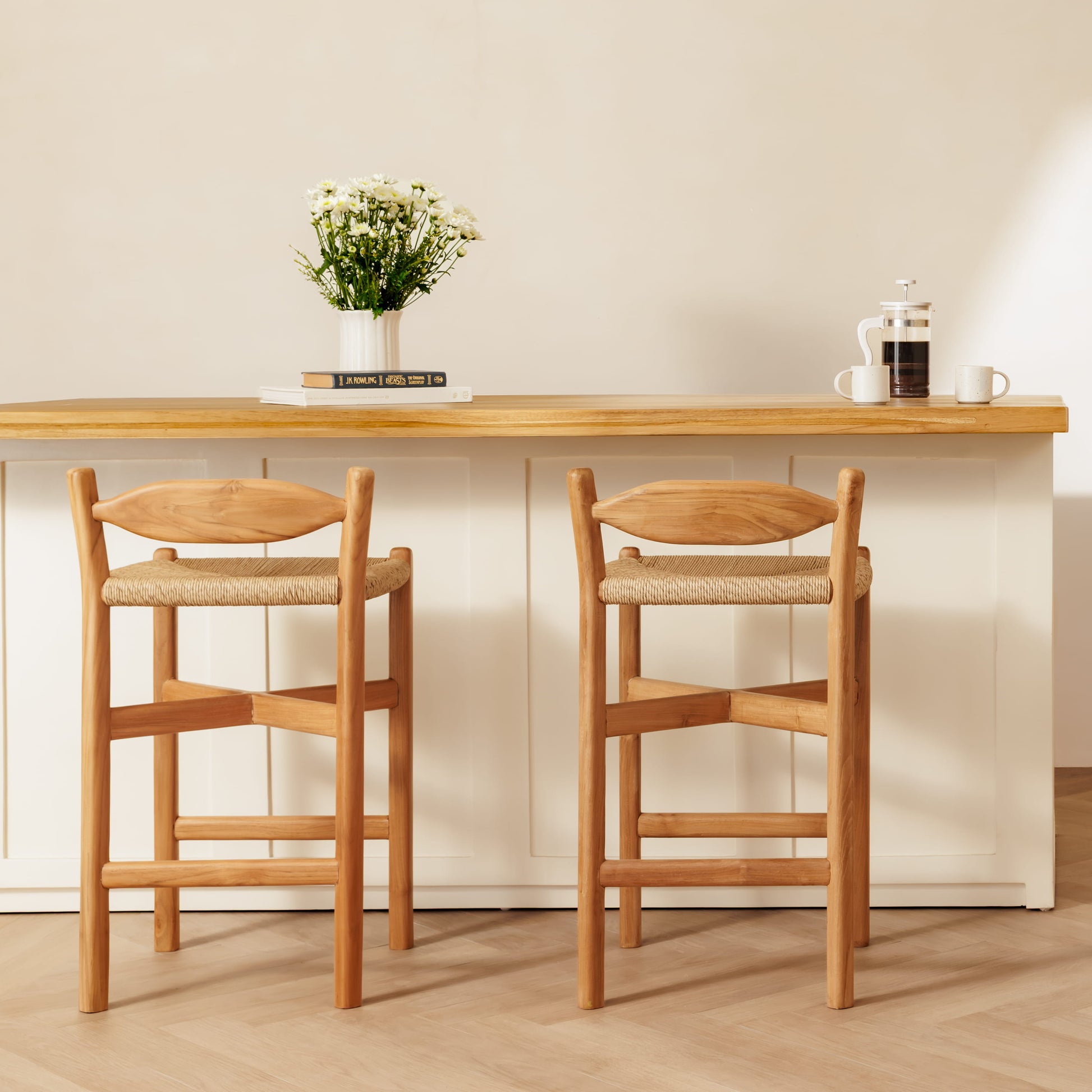 Two wooden bar stools with woven seats positioned in front of a light wood-topped counter in a bright, modern interior.