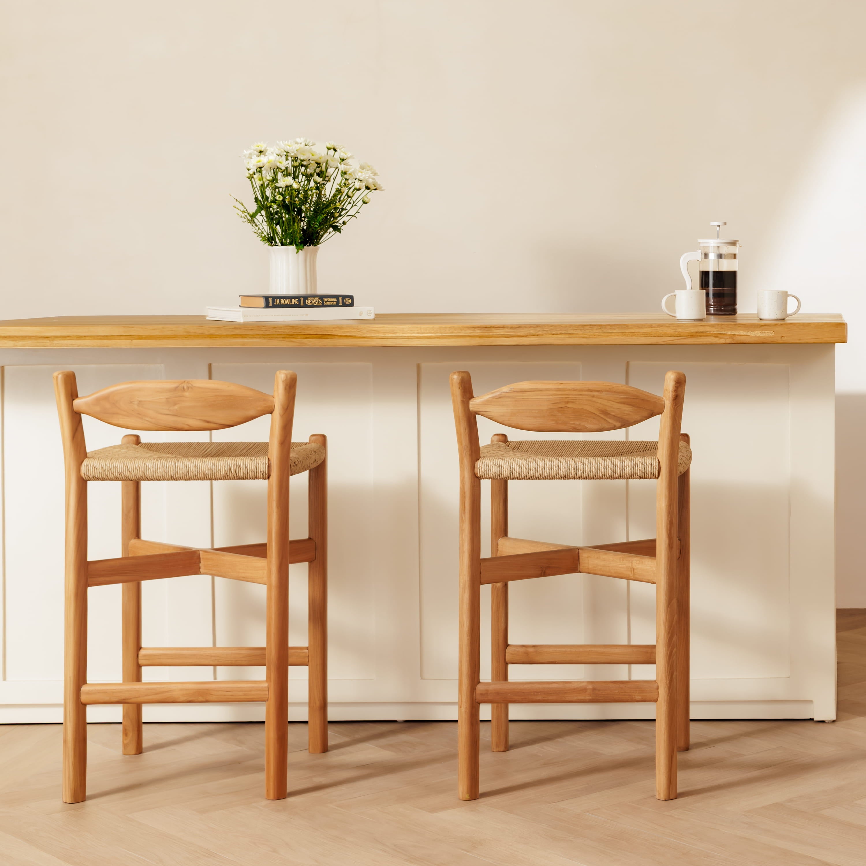 Two wooden bar stools with woven seats positioned in front of a light wood-topped counter in a bright, modern interior.
