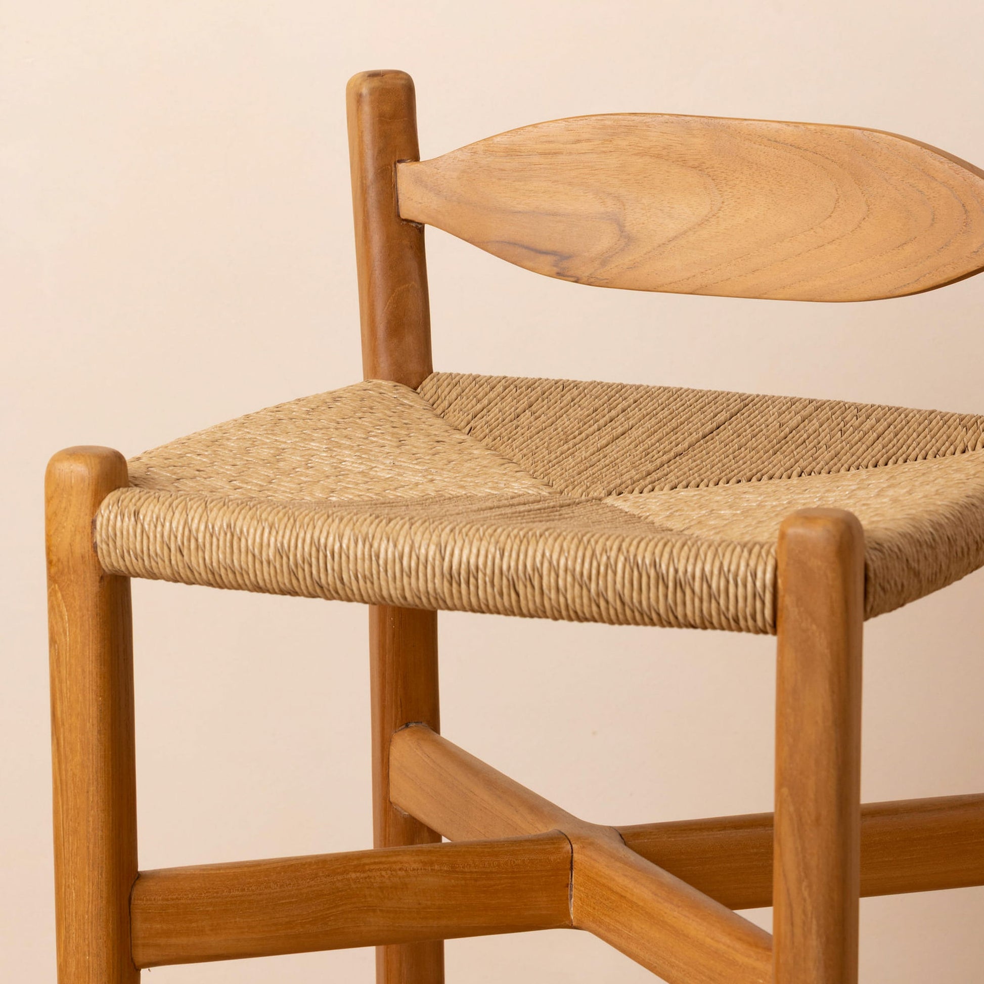 A close-up of a wooden chair with a natural woven rope seat and a curved wooden backrest, shown against a plain light beige background.