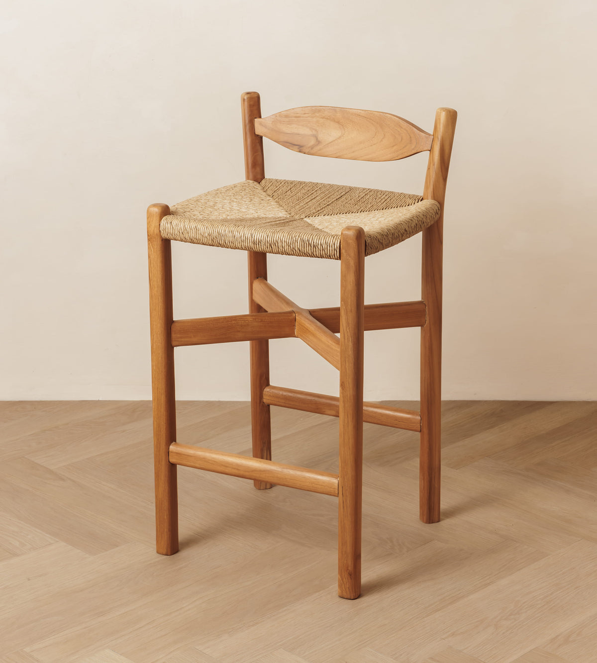 A wooden bar stool with a woven rope seat and a curved wooden backrest, shown in a minimalist room setting with a light beige wall and wood-look floor.