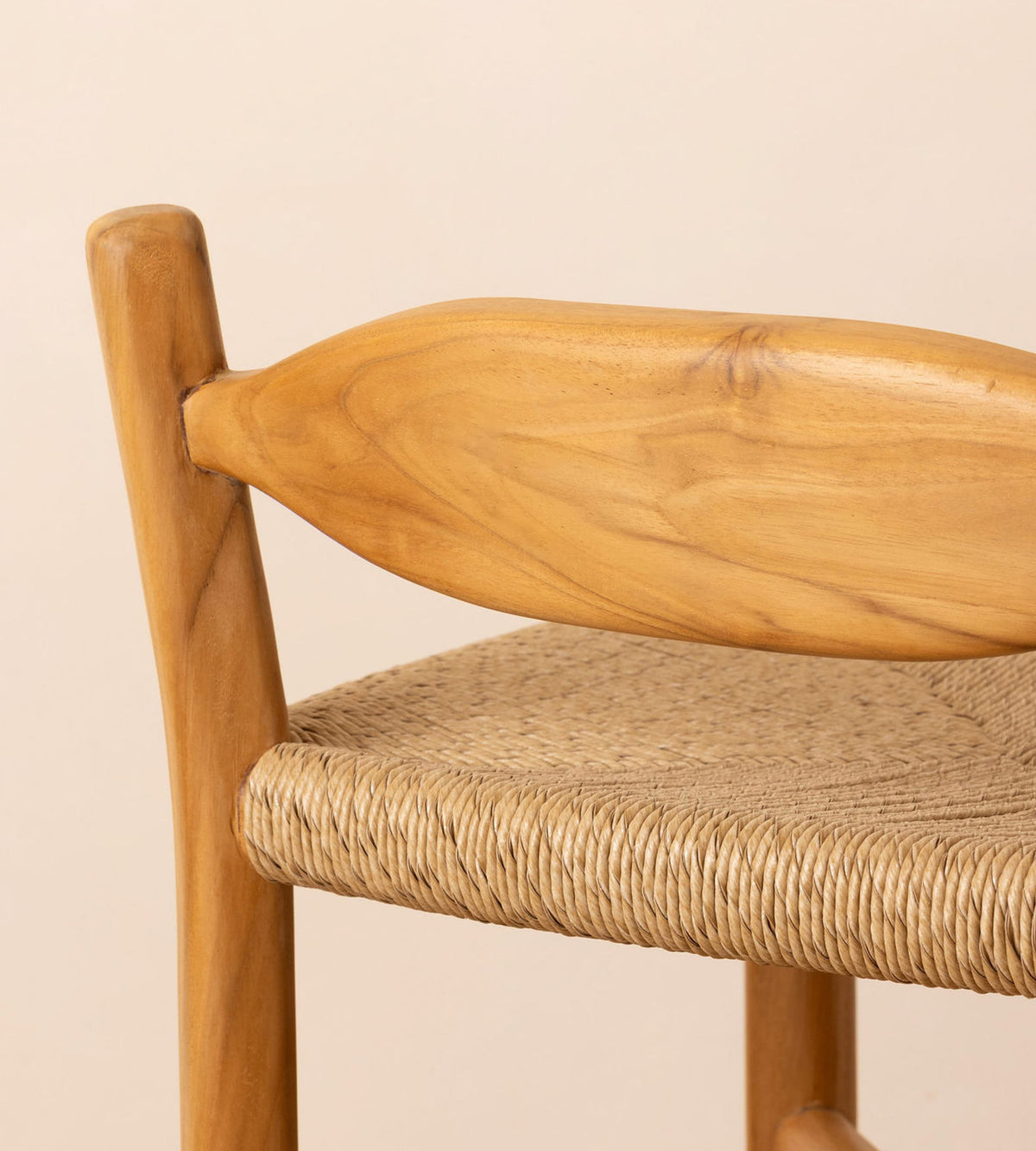 Close-up of a wooden chair with a curved natural wood backrest and a woven rope seat, shown against a plain light beige background.