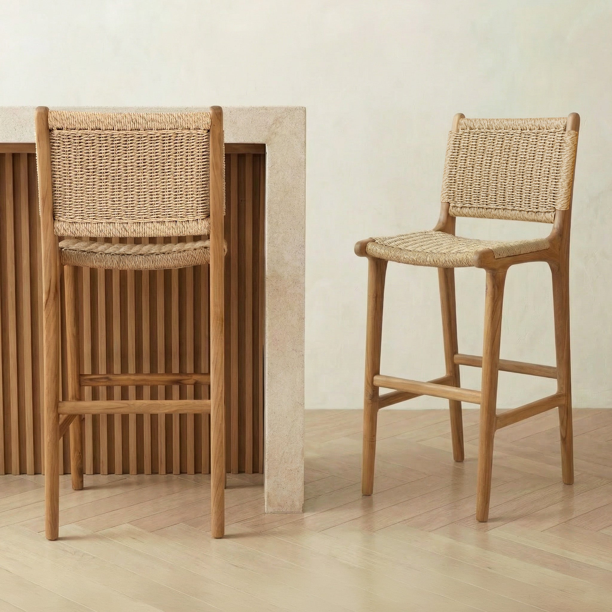 Two wooden bar stools with woven seats and backs against a plain wall.