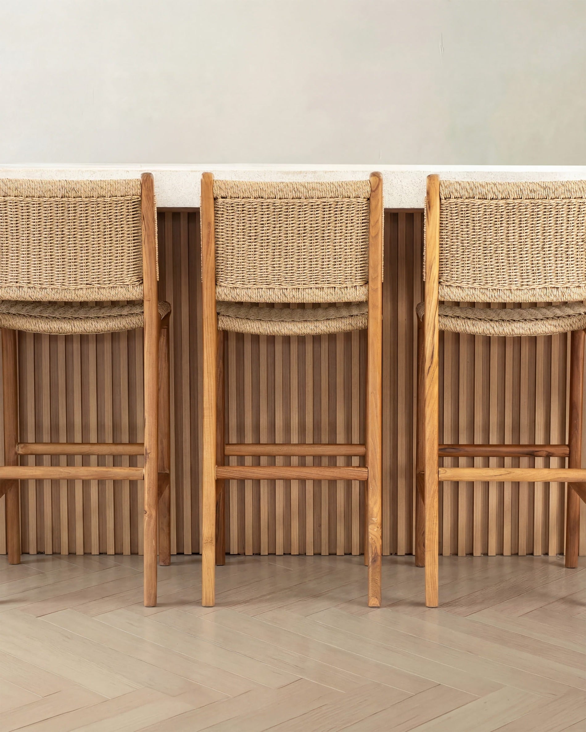Three wooden bar stools with woven backrests against a neutral wall.