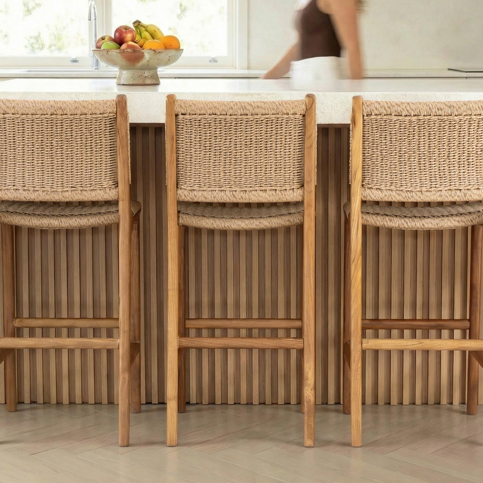 Three wicker bar stools in front of a kitchen counter with a blurred person in the background.