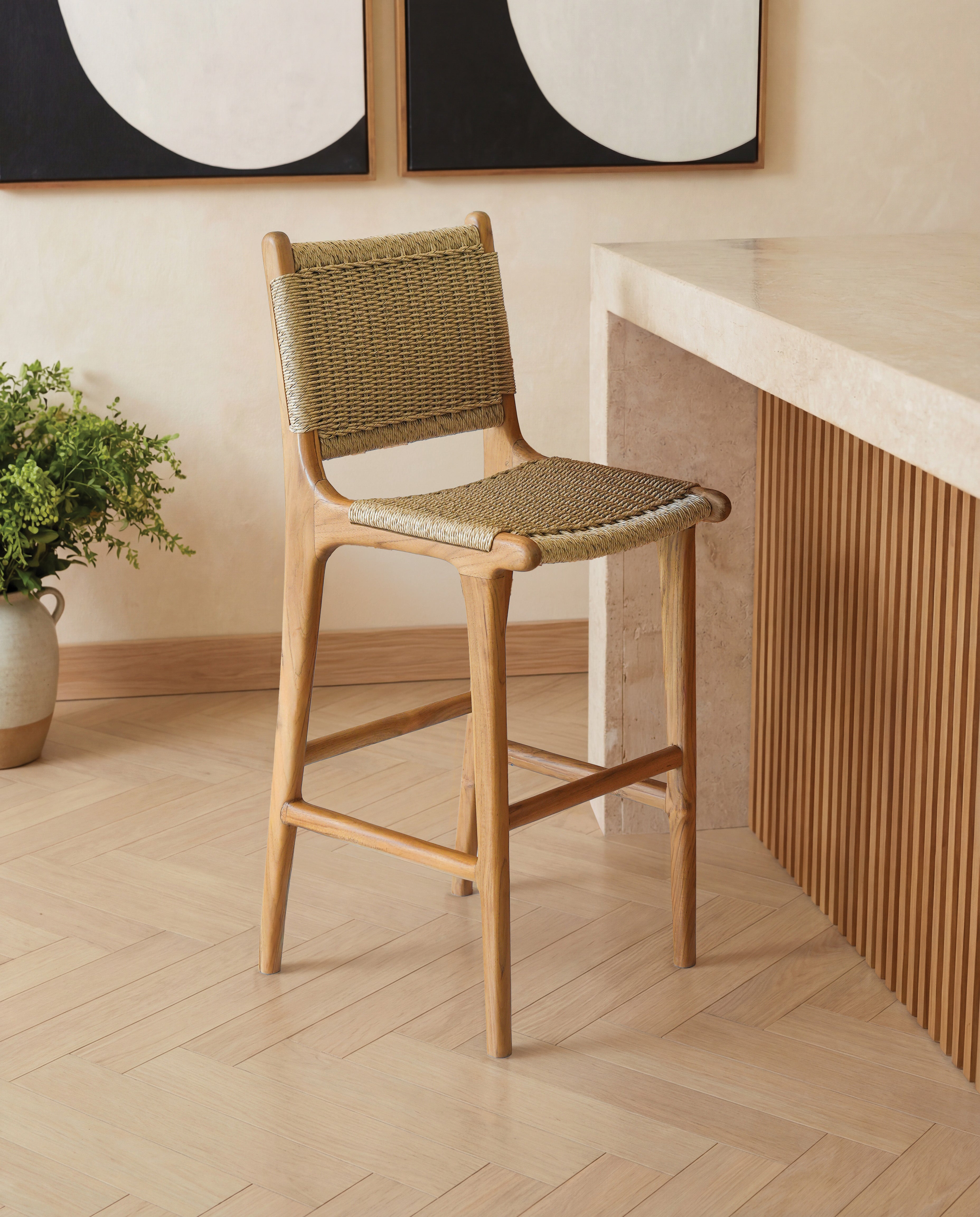 Woven bar stool in a room with a desk and framed artwork on the wall.