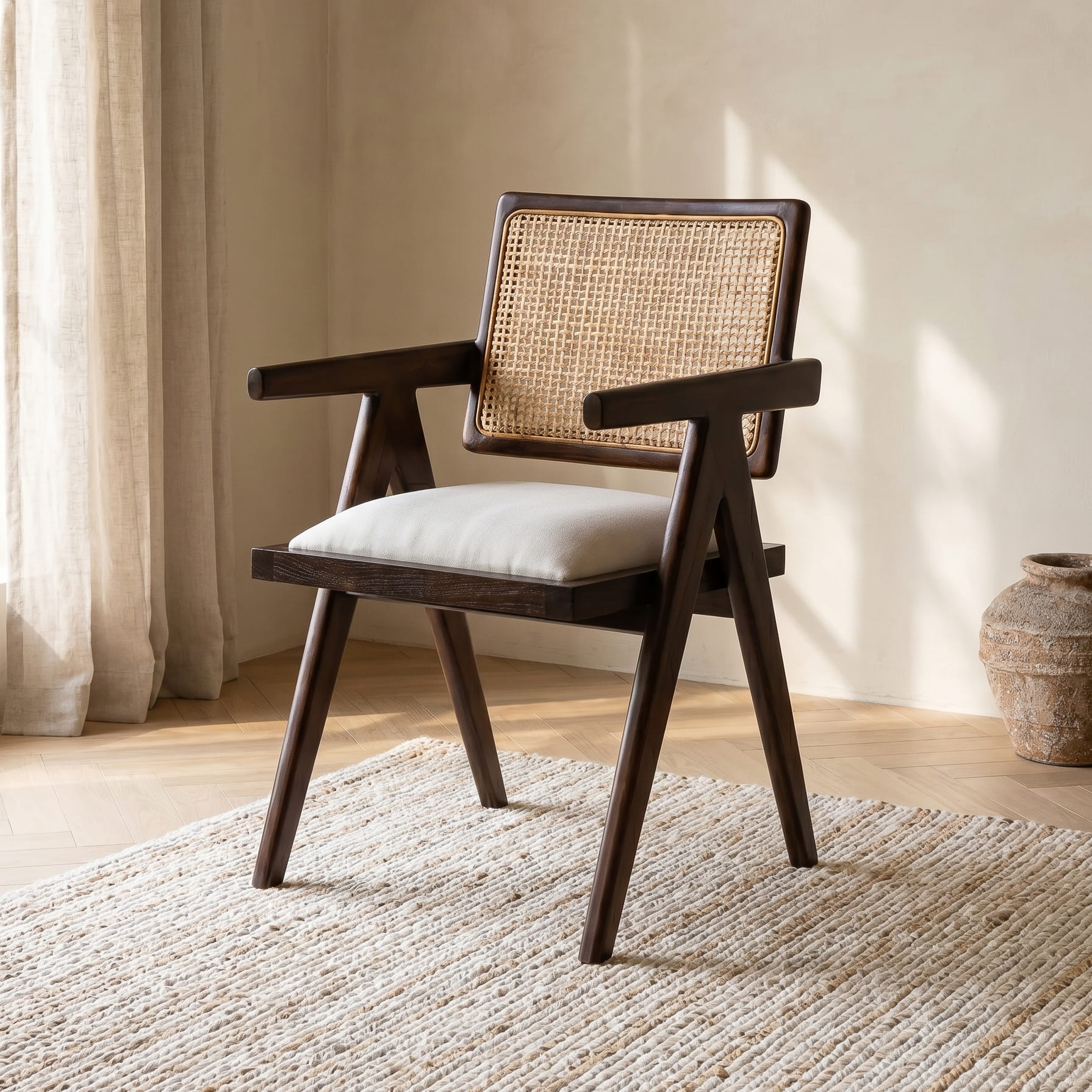 Wooden armchair with wicker backrest and white cushion in a room with curtains and a vase.