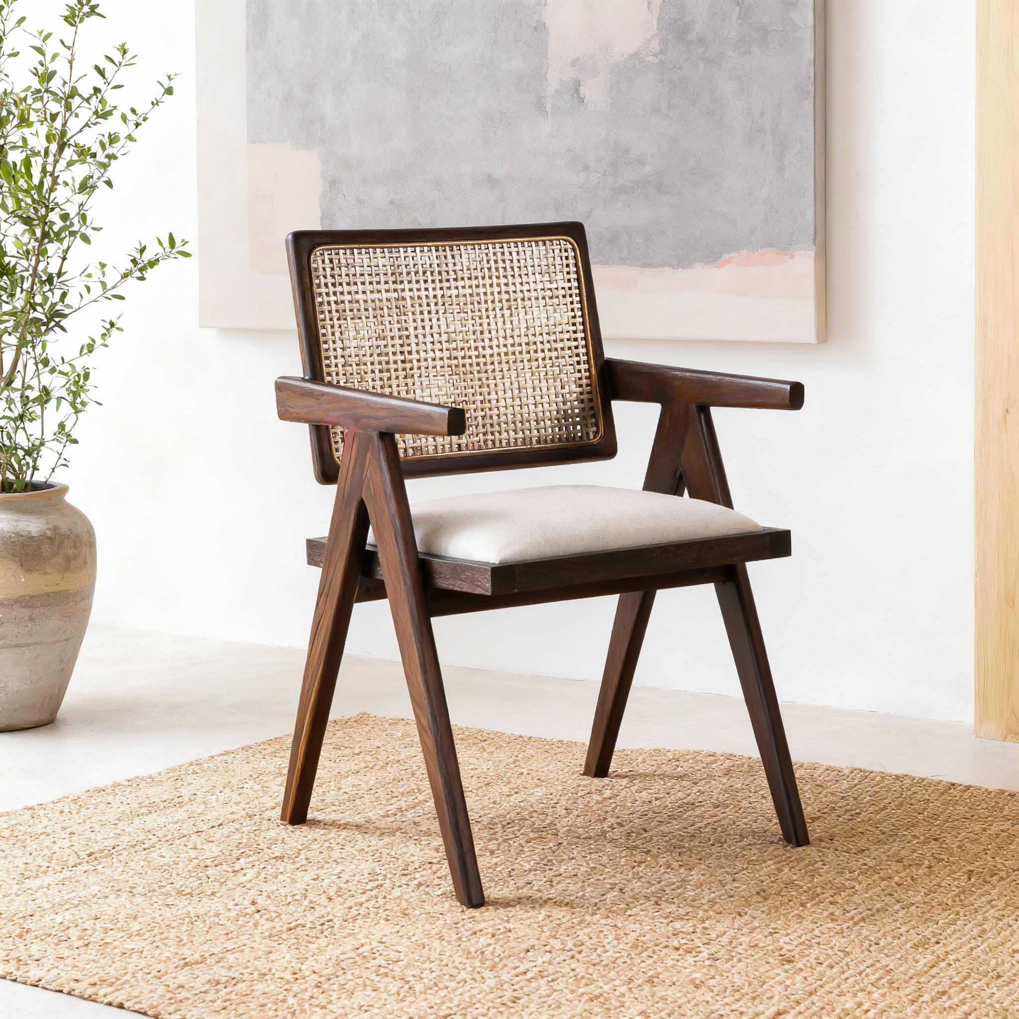 Wooden armchair with woven backrest in a room with a plant and abstract painting.