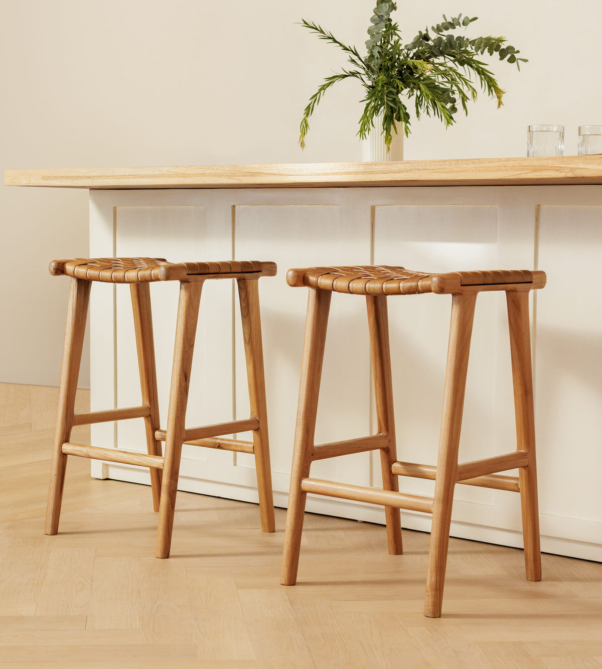 Two wooden bar stools with woven rope seats placed in front of a light wood counter in a bright, minimalist interior.