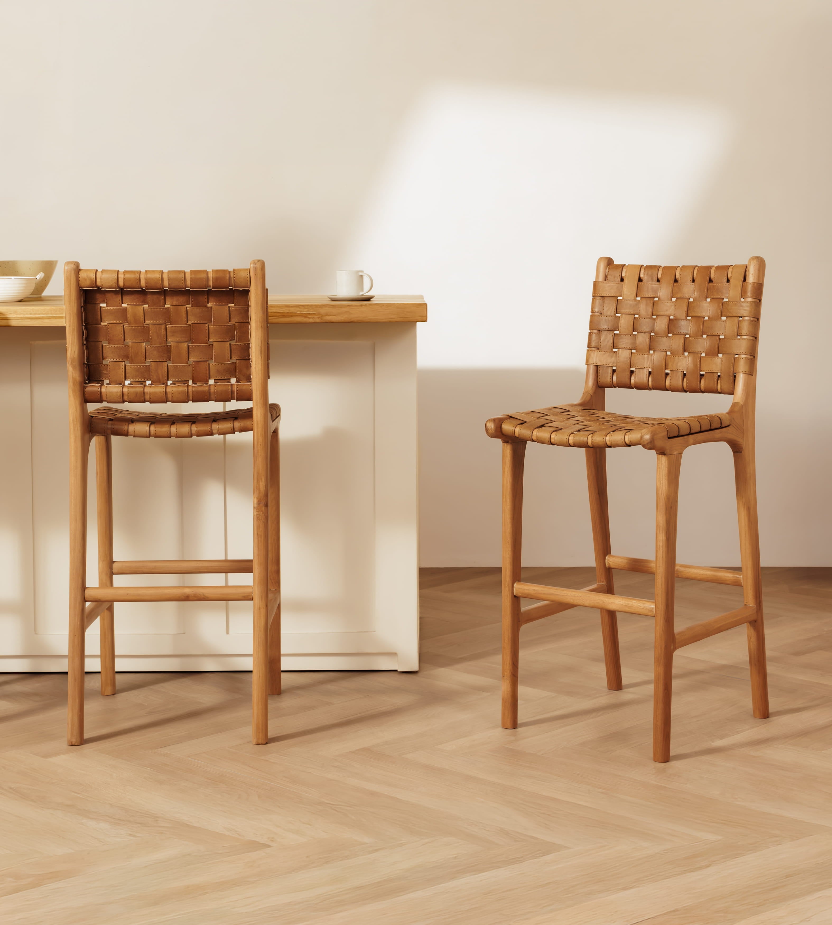 Two leather bar stools, shown in a bright, modern kitchen setting with a light wood counter and herringbone floor.