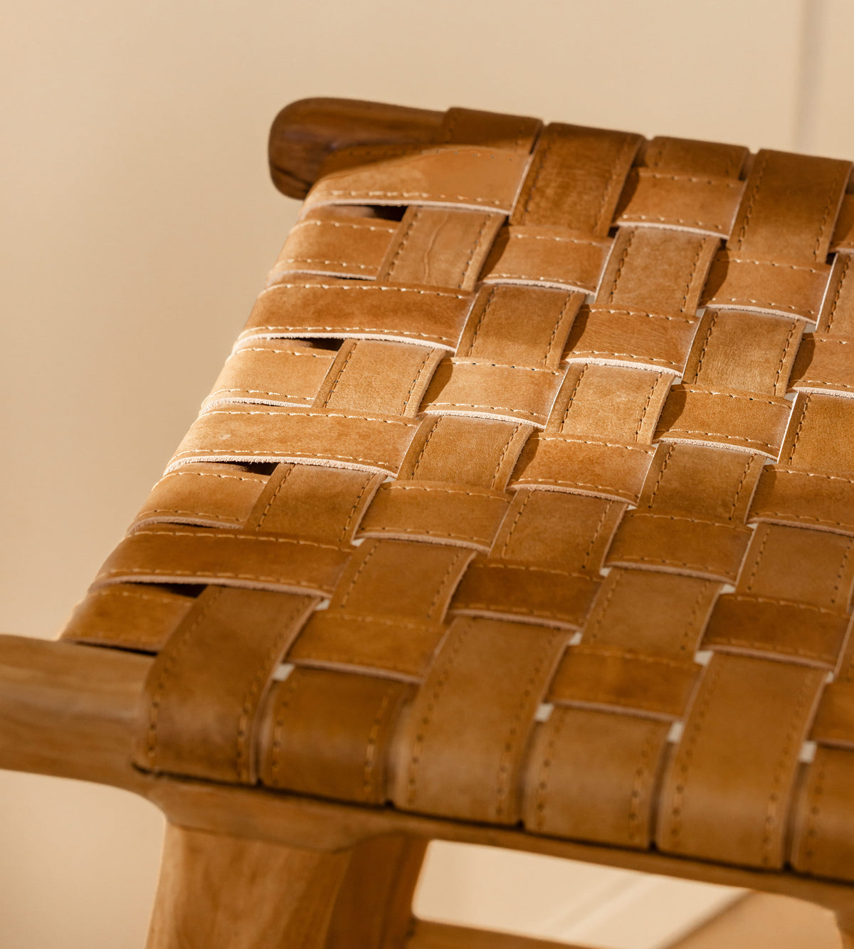 Close-up of a woven leather seat in warm tan and brown tones on a wooden chair, with a softly blurred beige background.