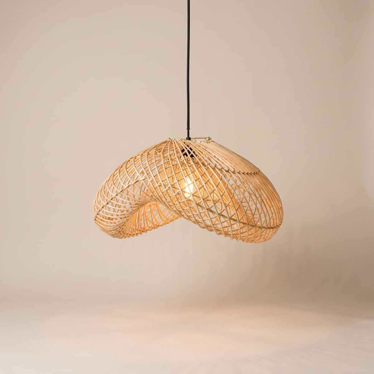 A modern pendant light with a curved, woven rattan shade suspended from a black cord against a warm beige background.