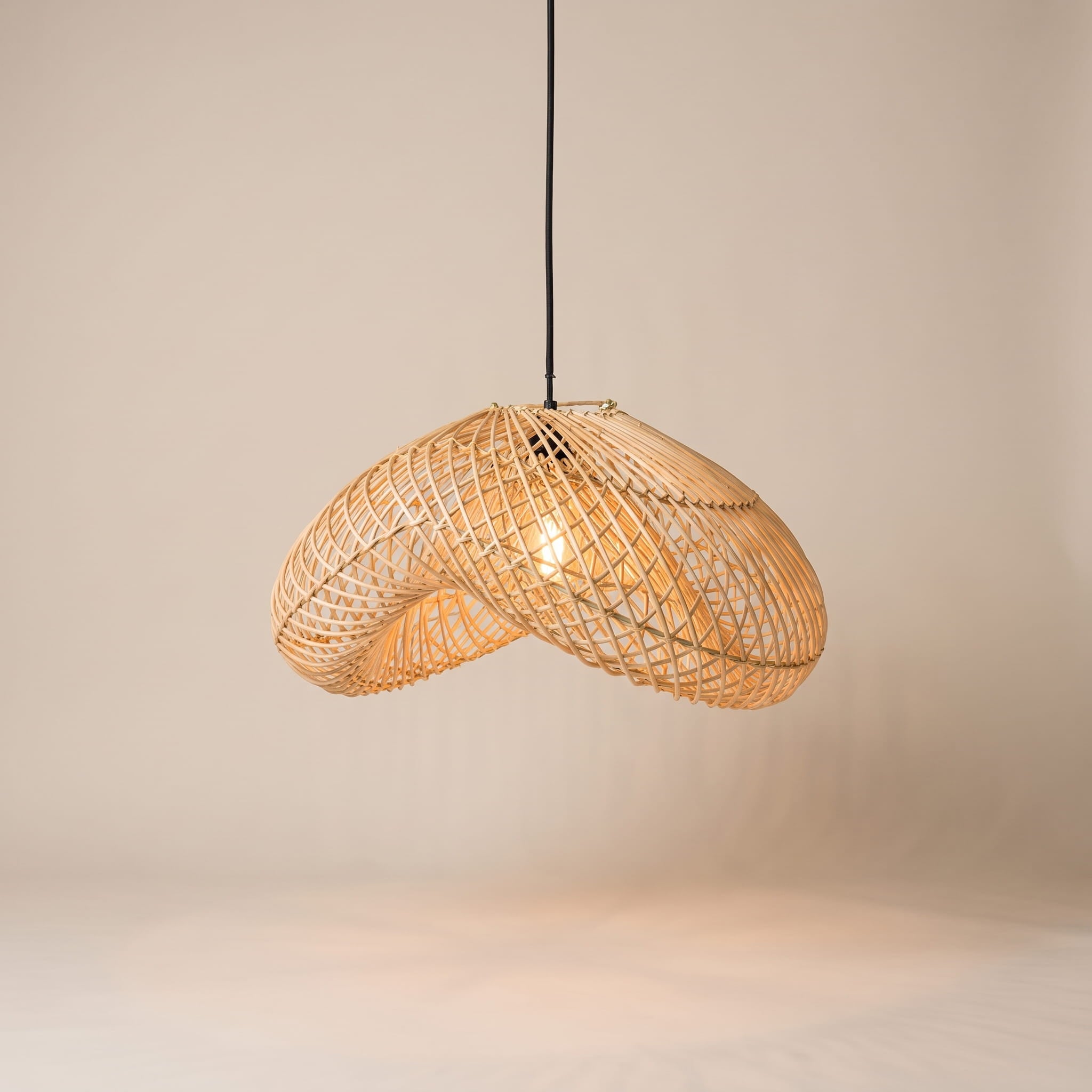 A modern pendant light with a curved, woven rattan shade suspended from a black cord against a warm beige background.