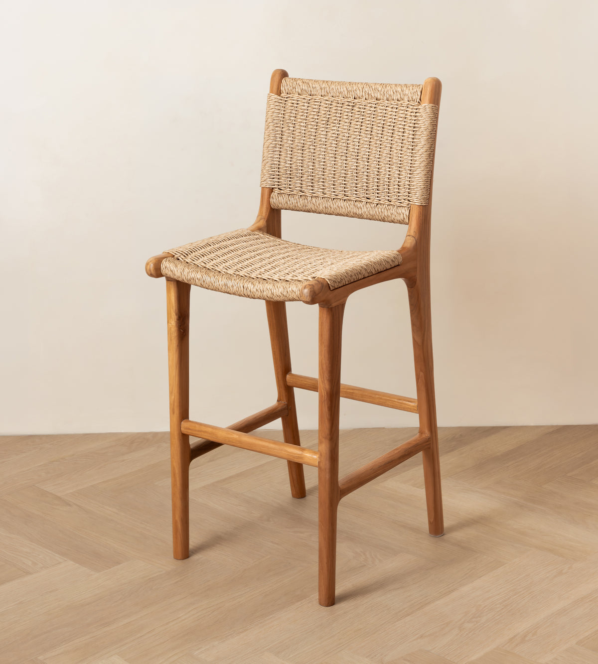 A wooden bar stool with a woven rattan seat and backrest, shown in a minimalist room setting with a light beige wall and wood-look floor.