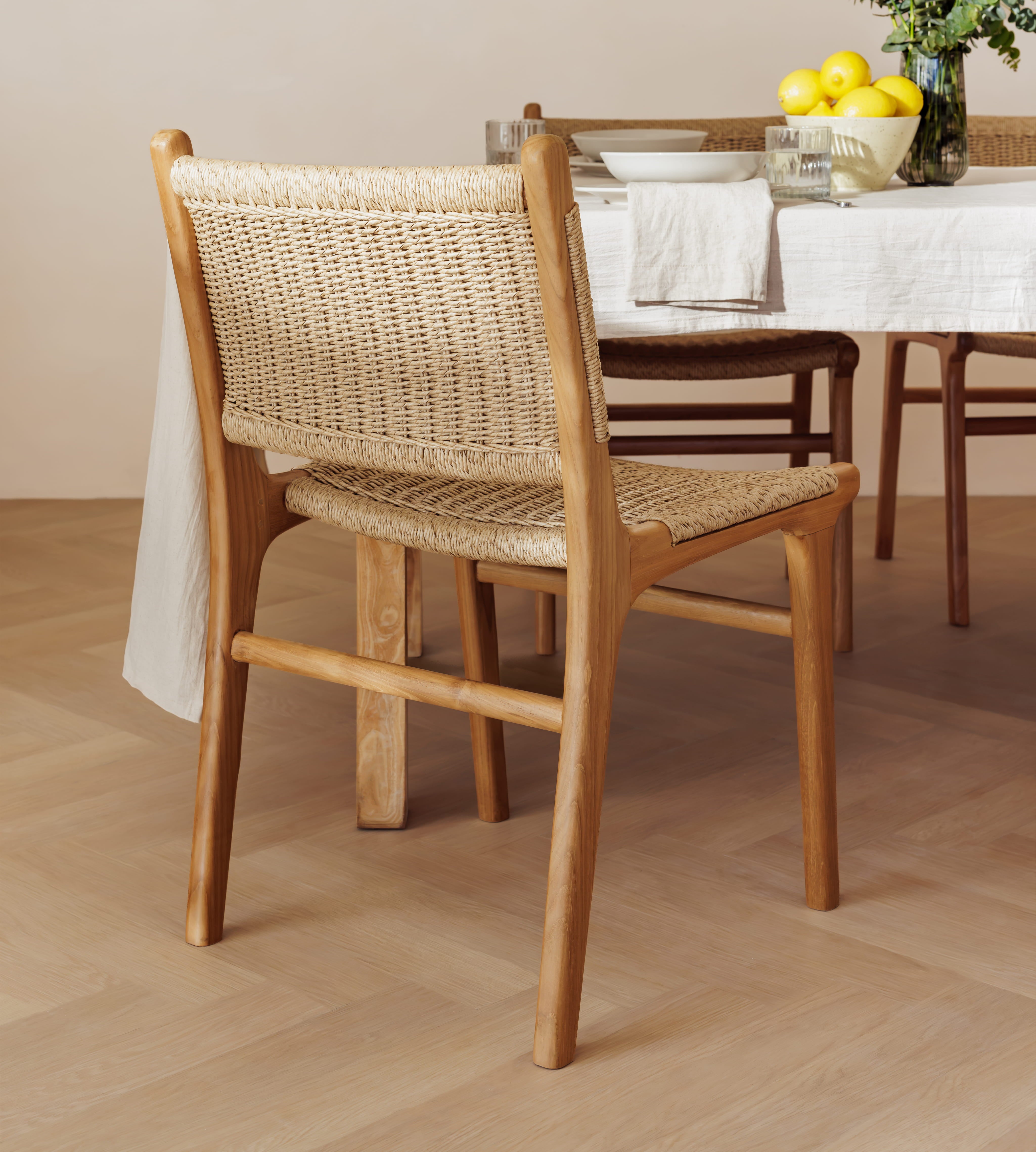 A wooden dining chair with a woven cane back and seat, shown in a dining room setting next to a table with a white tablecloth and yellow lemons.
