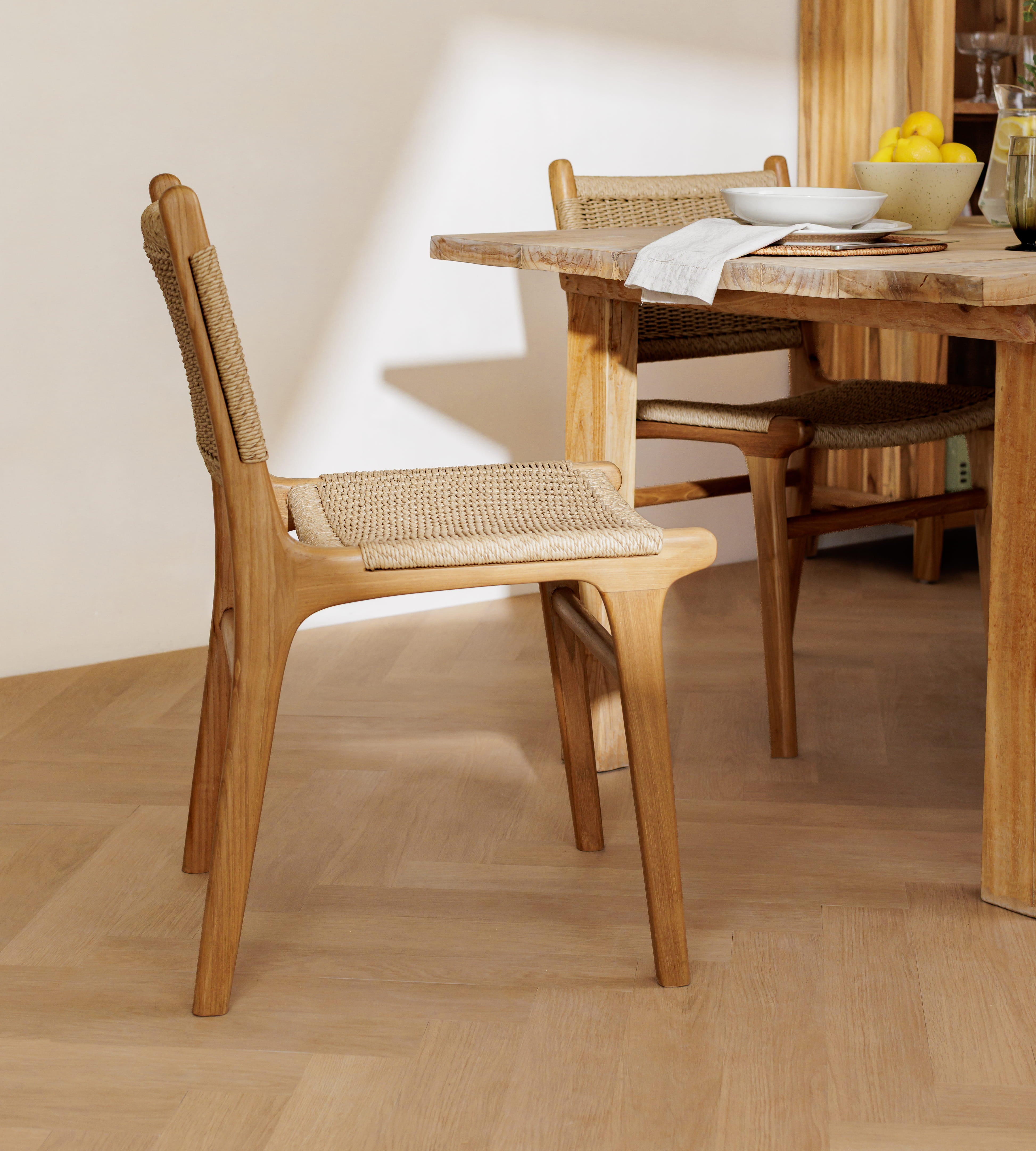 A wooden dining chair with a woven cane seat and back is shown in a bright, modern dining room next to a matching wooden table.