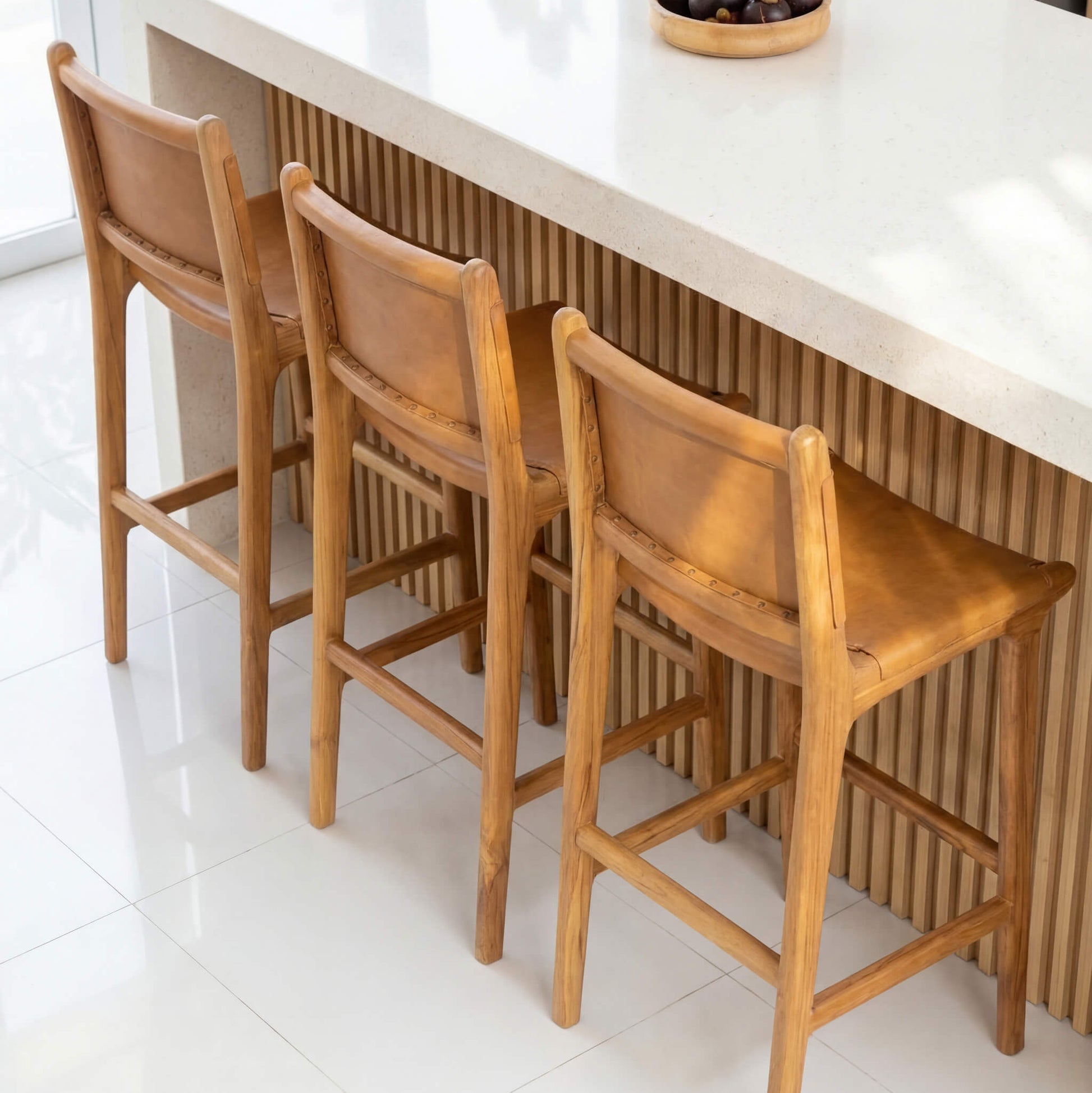 Three wooden bar stools in a kitchen setting with a white countertop.