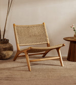 A rattan accent chair chair with a natural wood frame and woven rattan backrest, styled in a warm, minimalist room with a woven rug, a potted plant, and a small wooden side table.