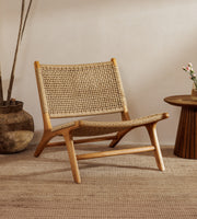 A rattan accent chair chair with a natural wood frame and woven rattan backrest, styled in a warm, minimalist room with a woven rug, a potted plant, and a small wooden side table.