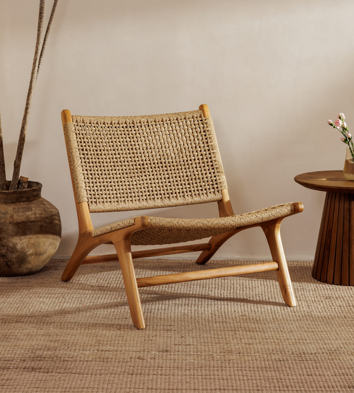 A rattan accent chair chair with a natural wood frame and woven rattan backrest, styled in a warm, minimalist room with a woven rug, a potted plant, and a small wooden side table.