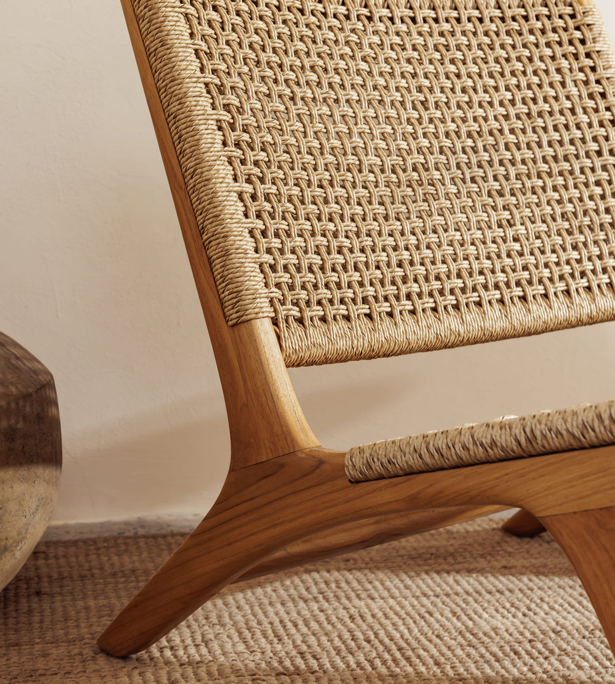 Close-up of a mid-century modern wooden lounge chair with woven cane or rattan seat and back, shown in a warm neutral interior setting.
