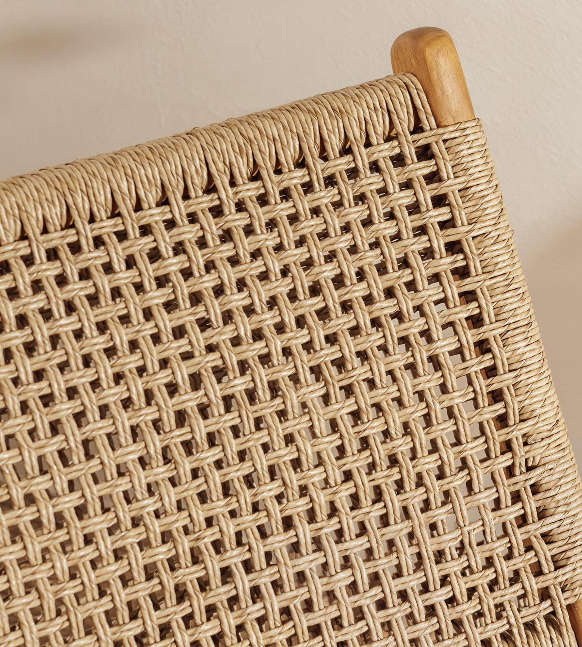 Close-up of a woven natural fiber chair seat with a light wood armrest against a warm beige background.